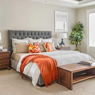 A modern bedroom with stylish decor, featuring a comfortable bed adorned with colorful pillows and a vibrant orange blanket.