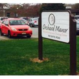 A parking lot with a sign for Orchard Manor and a red car parked nearby.