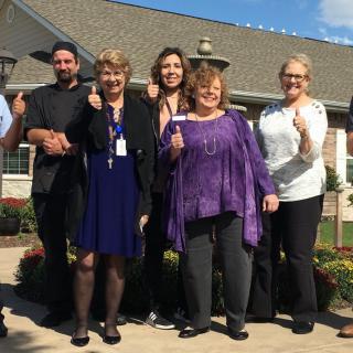A group of people standing outside, smiling and giving a thumbs-up gesture.