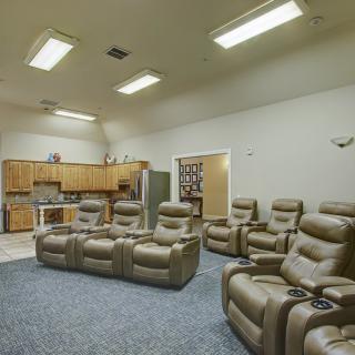 A cozy home theater setup with multiple recliner chairs and an adjoining kitchen area.