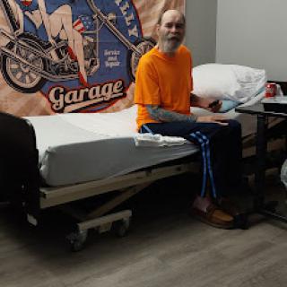 A patient sitting on a hospital bed, smiling in an orange shirt and blue pants.