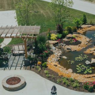 A beautifully landscaped garden featuring a pond, pergola, and fire pit area.