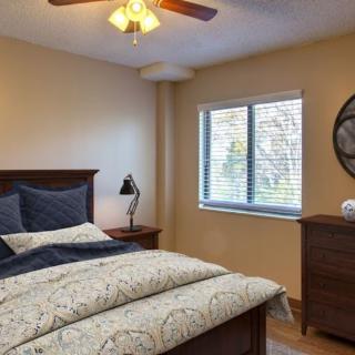 A cozy bedroom with a wooden bed, patterned bedding, a lamp, and a window with blinds.
