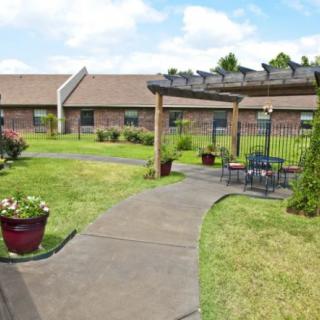 A garden with a pathway and outdoor seating under a pergola, set in front of a building.