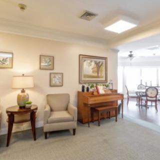 A cozy living room features a piano, artwork on the walls, and comfortable seating.