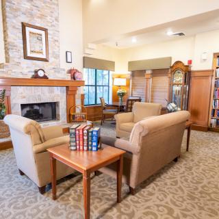 A cozy living room with a fireplace and armchairs, decorated with books and a grandfather clock.