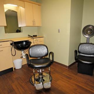 Interior of a hair salon featuring a styling chair, sink, mirror, and hair dryer.