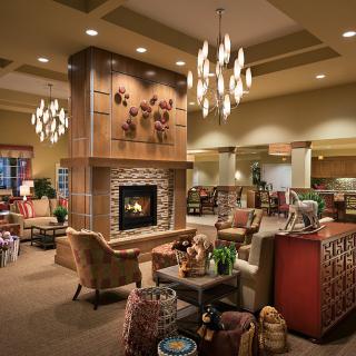 A cozy living room with a central fireplace, surrounded by comfortable furniture and illuminated by elegant chandeliers.