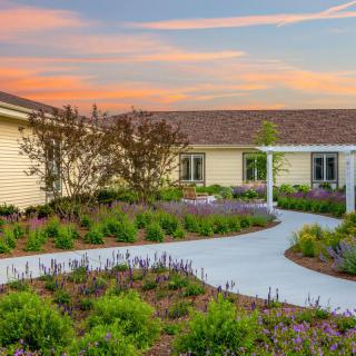 A beautiful garden path leads to a cozy house under a colorful sunset sky.
