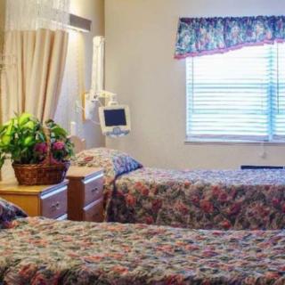 A hospital room featuring two beds and a monitor, decorated with floral curtains and a basket of flowers.