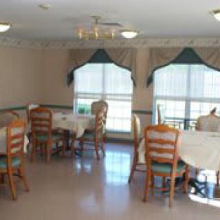 A dining area with multiple tables and chairs, featuring large windows with curtains.