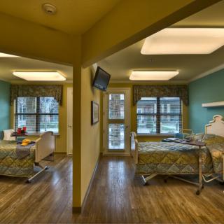 A hospital room with two patient beds, each having its own window and television.
