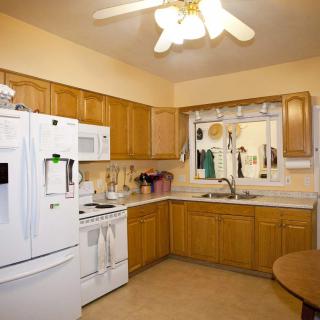A cozy kitchen featuring wooden cabinets, a white refrigerator, and a microwave with a ceiling fan above.