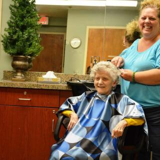 An older woman getting a haircut by a smiling hairstylist in a salon.