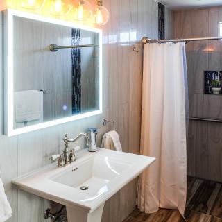 A modern bathroom with a well-lit mirror, sink, and shower area.