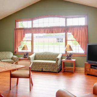 A cozy living room with a sofa set, television, and large windows with curtains.