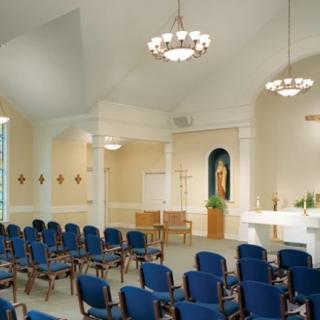 A serene chapel interior featuring rows of blue chairs, an altar, and elegant lighting fixtures.