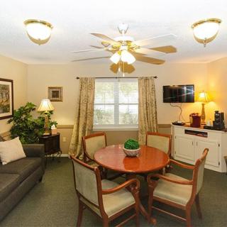 A cozy living room with a round table, chairs, a sofa, and a ceiling fan.