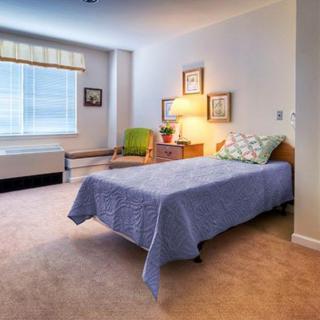 A cozy bedroom with a single bed, armchair, and a warm lamp by the window.