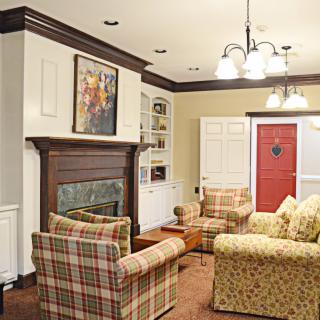 A cozy living room with a fireplace, plaid chairs, and a red door.