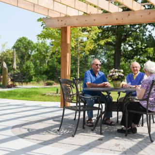 A group of seniors enjoying a conversation under a pergola in a garden setting.