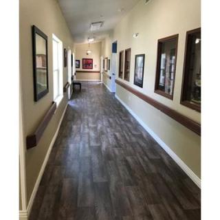 A long hallway with wooden flooring, decorated with artwork on the walls and illuminated by natural light through windows.