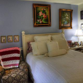 A cozy bedroom with a bed, decorative pillows, artwork on the walls, and a lamp on the bedside table.