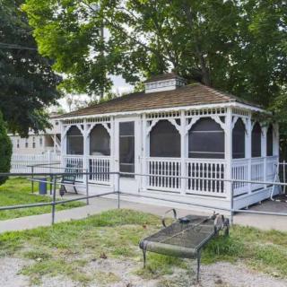 A white gazebo surrounded by trees with a bench in the foreground.