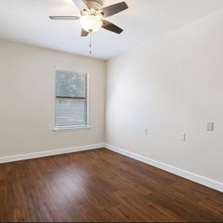 A spacious empty room with wood flooring, a ceiling fan, and a window.