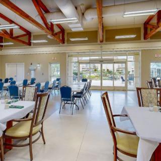A spacious dining hall with neatly arranged tables and chairs, featuring glass doors that allow natural light to fill the room.