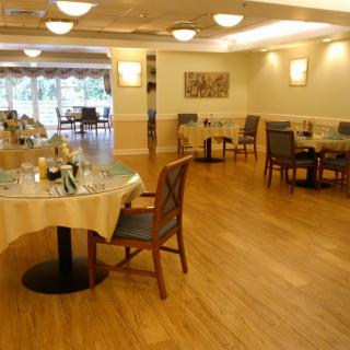A well-lit restaurant dining area featuring wooden floors and neatly arranged tables and chairs.