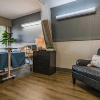 A modern hospital room with a comfortable chair and a bedside lamp.