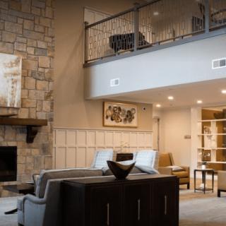 A modern living room with a stone fireplace, cozy seating, and an open balcony.