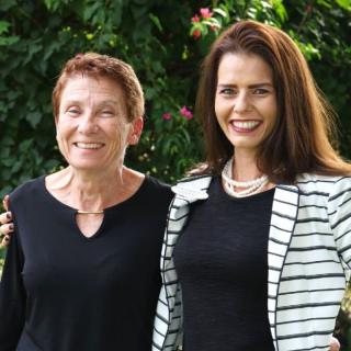 Two women smiling outdoors in a garden setting.