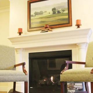 Cozy interior with a fireplace, two chairs, and a painting above the mantel.