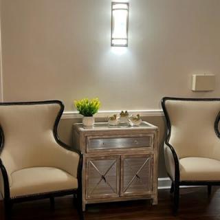 A cozy seating area with two elegant chairs and a decorative table, softly lit by a wall sconce.