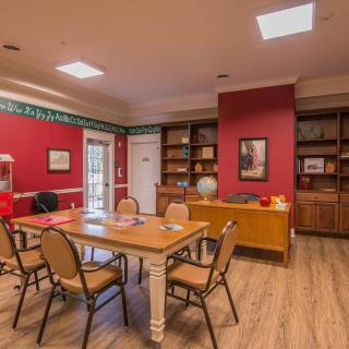 A cozy meeting room with red walls, a wooden table surrounded by chairs, and bookshelves filled with decorative items.