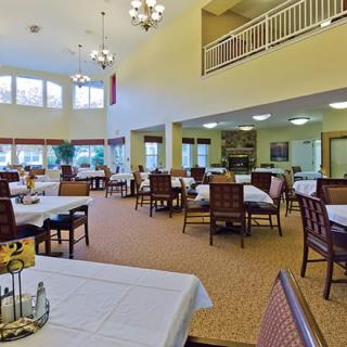 A spacious dining area with multiple tables and chairs, featuring bright lighting and large windows.