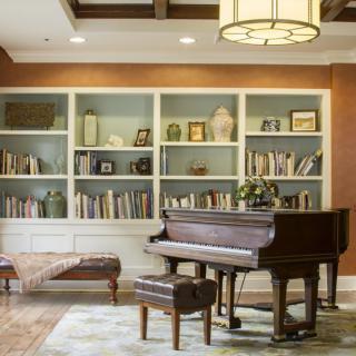 A cozy living room featuring a grand piano and bookshelves filled with books.