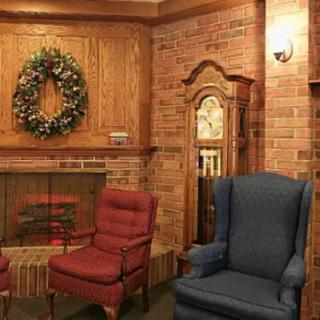 A cozy living room with a fireplace, featuring brick walls and comfortable armchairs, adorned with a decorative wreath.