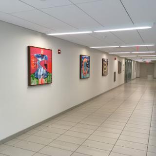 A well-lit hallway featuring various colorful paintings on the walls.