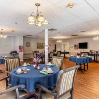 A cozy dining room setup with tables covered in blue tablecloths and striped chairs, featuring elegant lighting fixtures and a warm atmosphere.