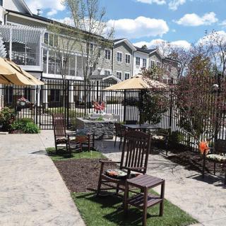 A peaceful outdoor patio area with chairs and umbrellas, surrounded by garden landscaping and adjacent buildings.