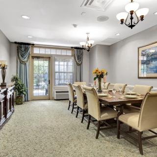 A beautifully decorated dining room with a long table and elegant chairs, adorned by a chandelier and large windows.
