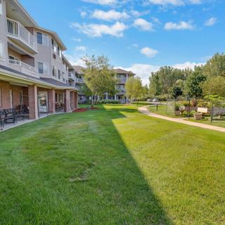 A view of an apartment complex with a well-maintained lawn and pathway, surrounded by trees under a clear blue sky.