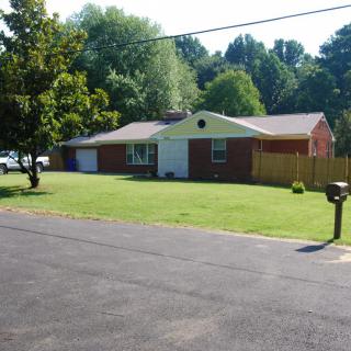 A suburban house with a neatly manicured lawn and surrounding trees on a sunny day.