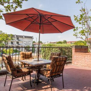 A sunny patio with outdoor furniture and an umbrella, overlooking greenery.