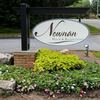 Entrance sign for Newman Health & Resort surrounded by blooming flowers and lush plants.