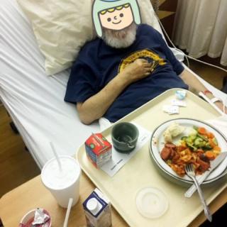 A patient in a hospital bed with a meal tray in front of them.