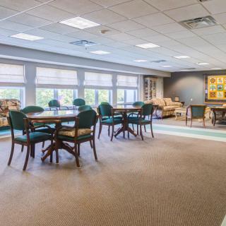 A spacious and well-lit room featuring multiple tables and chairs, with large windows allowing natural light to fill the space.